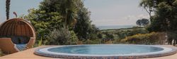 Outdoor round pool with wicker lounge chair surrounded by lush greenery and countryside view