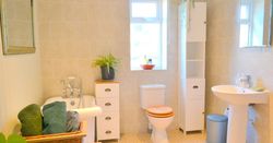 Bright bathroom with a white bathtub, sink, toilet, and storage units, decorated with plants and folded towels.
