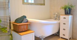 A bright bathroom featuring a clawfoot bathtub, wicker basket with towels, potted plant, and white drawers.