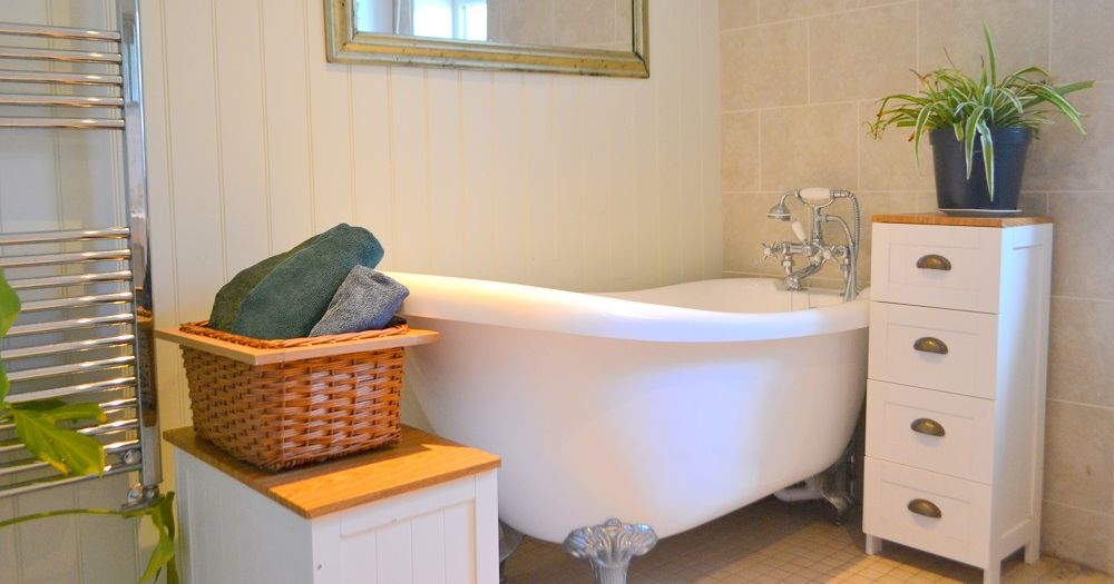 A bright bathroom featuring a clawfoot bathtub, wicker basket with towels, potted plant, and white drawers.