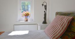Bright bedroom with a window, flowers in a vase on the sill, striped pillow and decorative lamp