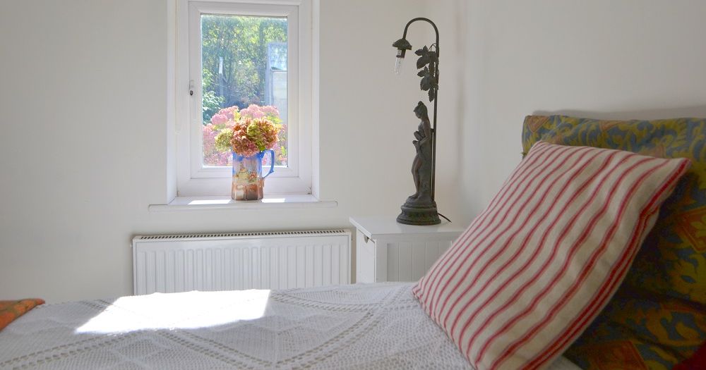 Bright bedroom with a window, flowers in a vase on the sill, striped pillow and decorative lamp