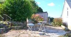 Sunny patio with two white metal chairs and a table surrounded by greenery