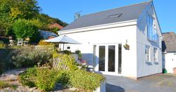 White cottage with patio seating and garden under a clear blue sky