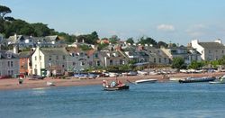 Shaldon ferry crossing the water with houses and boats on the shore in the background.