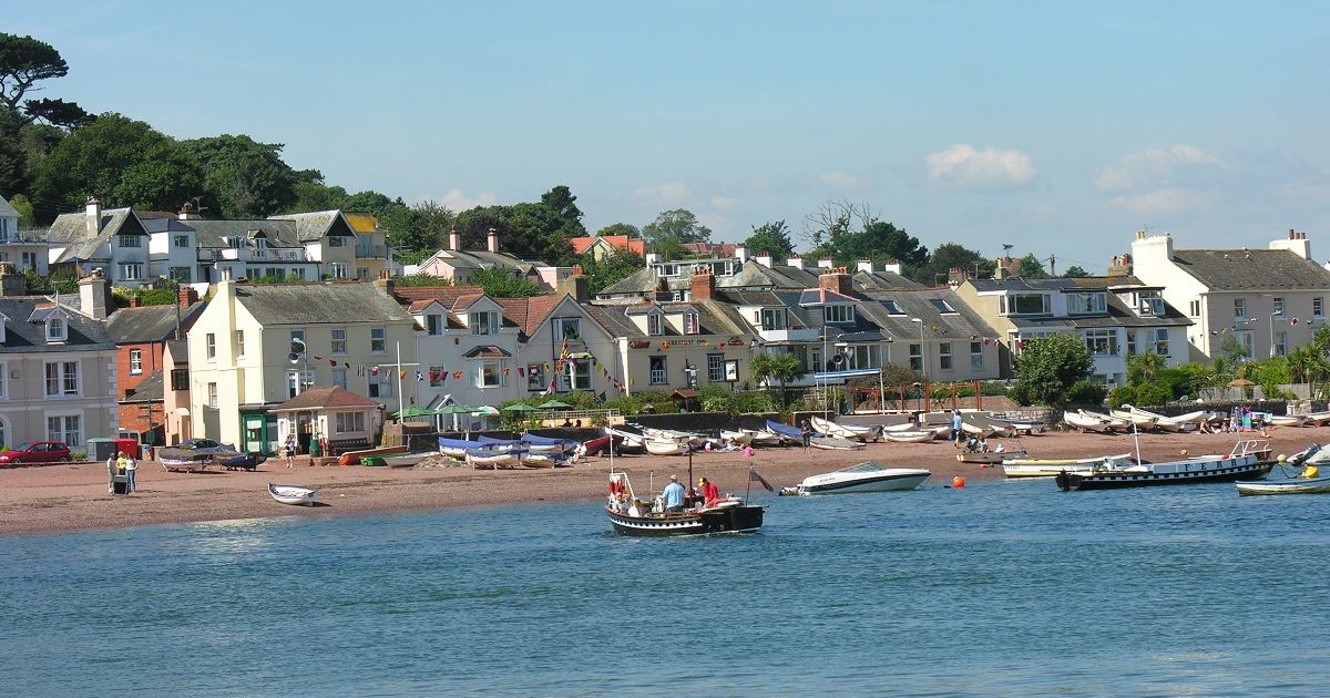 Shaldon ferry crossing the water with houses and boats on the shore in the background.