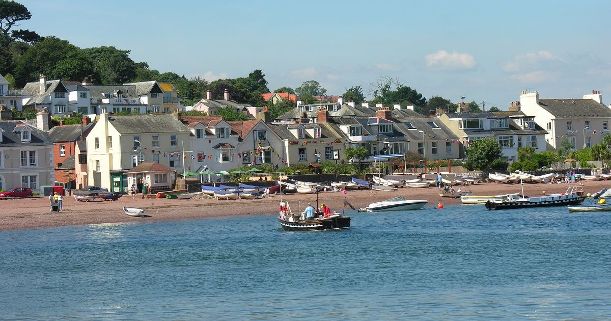 Shaldon ferry crossing the water with houses and boats on the shore in the background.