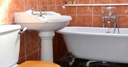 Bathroom with white toilet, pedestal sink, and clawfoot bathtub against orange tiles.