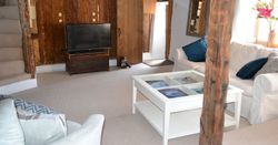 Cozy living room with exposed wood beams, rustic walls, a TV, white sofas, and a glass coffee table