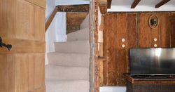 Interior of a rustic living room with wooden beams, staircase, and TV