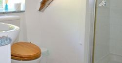 Rustic bathroom with exposed wooden beam, toilet with wooden seat, sink, shower and window.