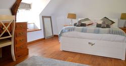 Cozy attic bedroom with a wooden floor, white bed, desk, and exposed wooden beams.
