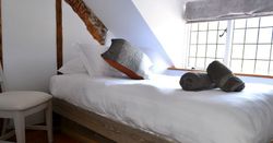 Cozy bedroom with a neatly made bed, decorative pillows, and two rolled towels on top, next to a window with natural light.