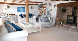 Cozy living room with exposed wooden beams, white sofas, a stone fireplace, bookshelves, and a desk.
