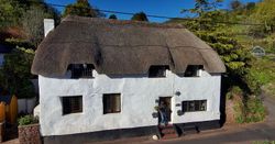 Traditional white thatched cottage with a person standing at the front door