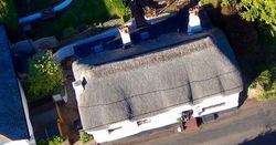 Aerial view of a thatched-roof cottage with a garden and patio area.