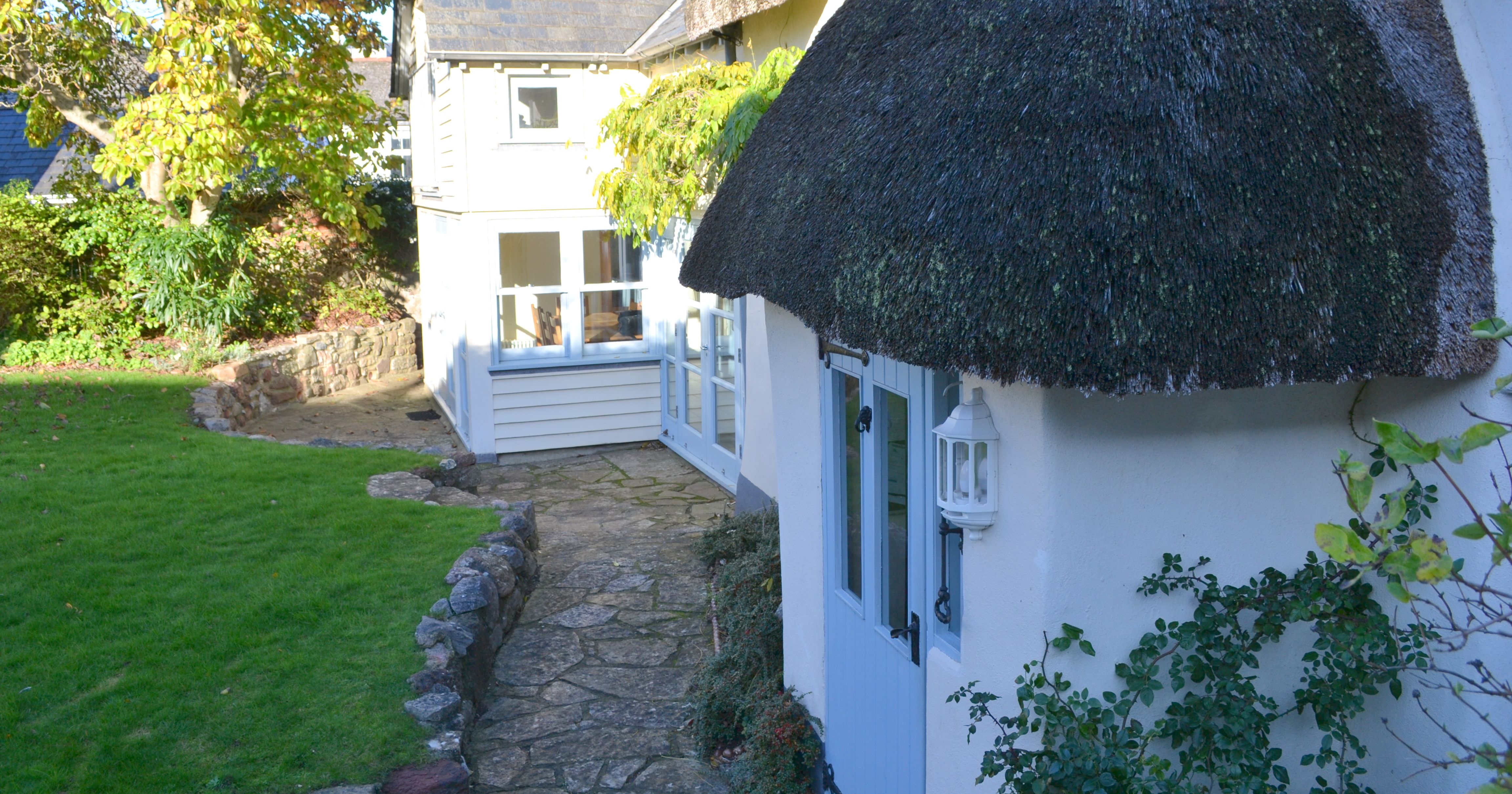 Traditional cottage with a thatched roof and a stone pathway, surrounded by a green garden.