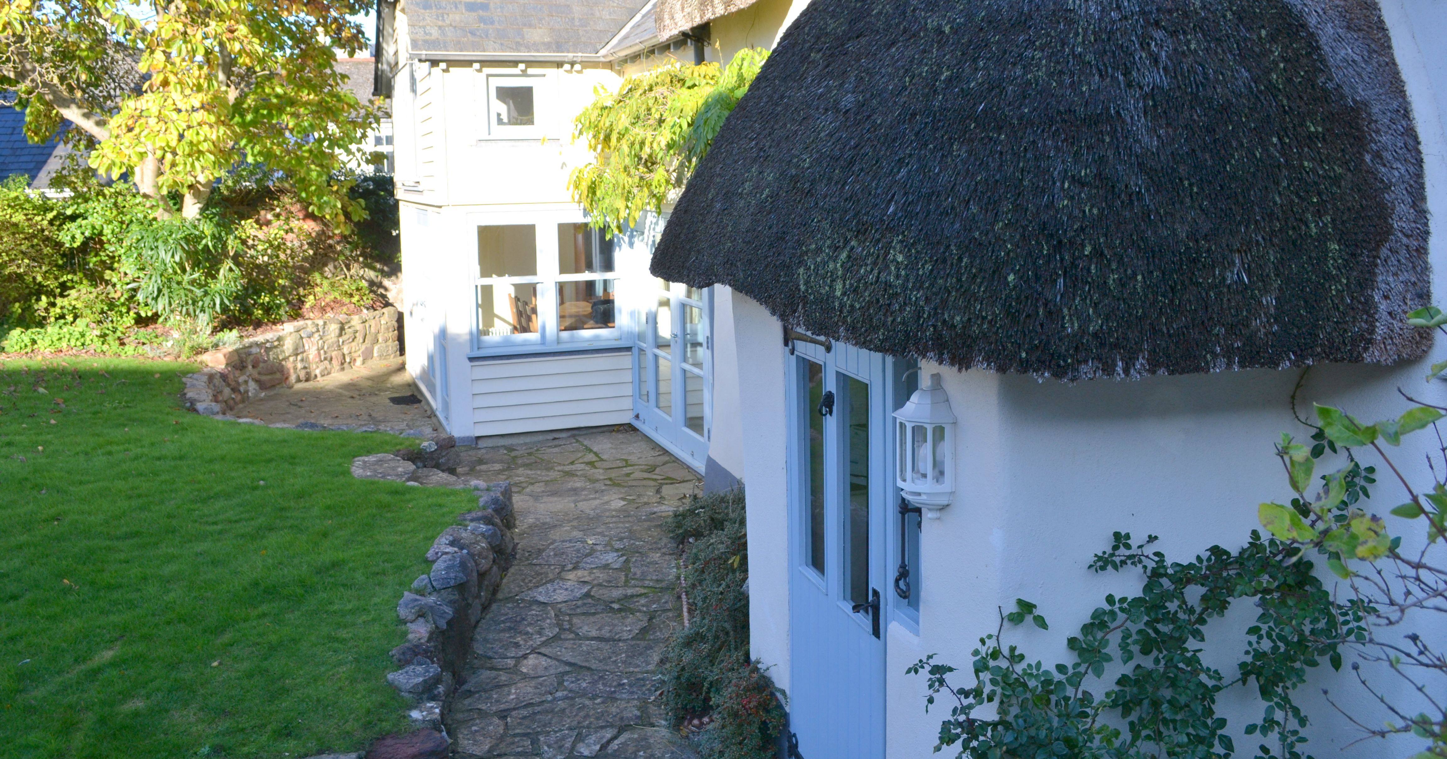 Traditional cottage with a thatched roof and a stone pathway, surrounded by a green garden.