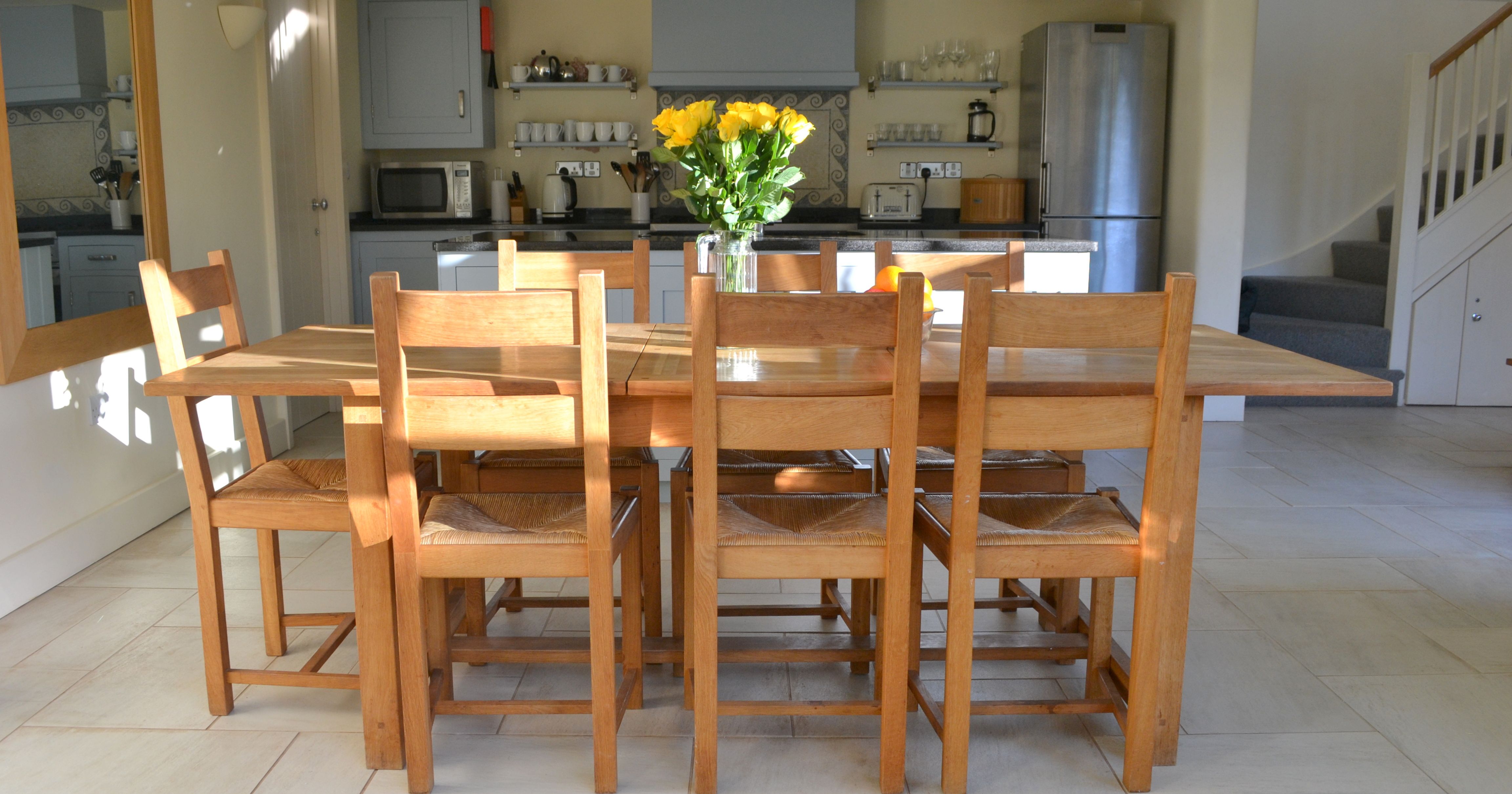 Wooden dining table with chairs and a vase of yellow flowers in a kitchen