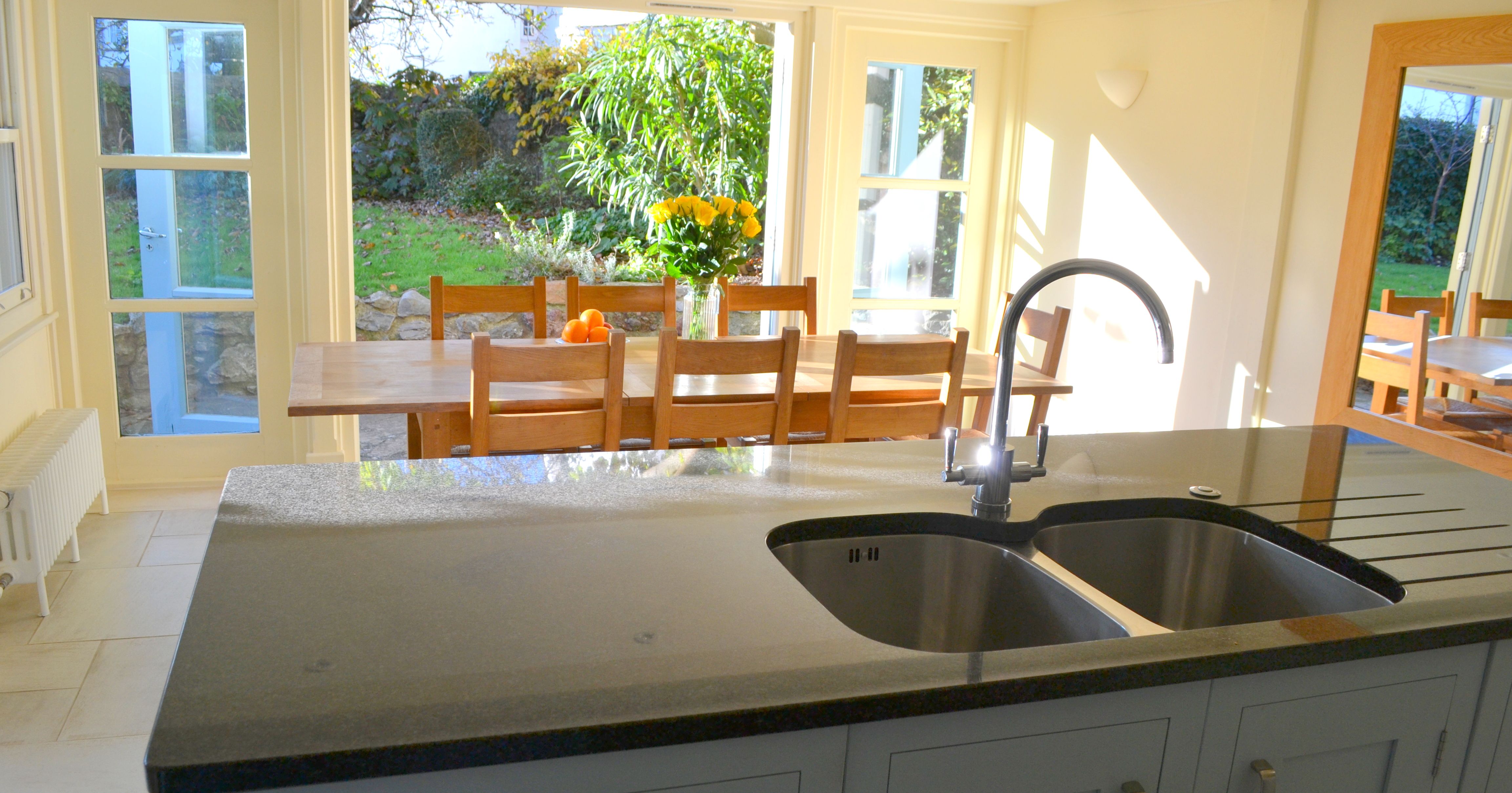 Modern kitchen with island sink and dining area with large windows overlooking a green garden.