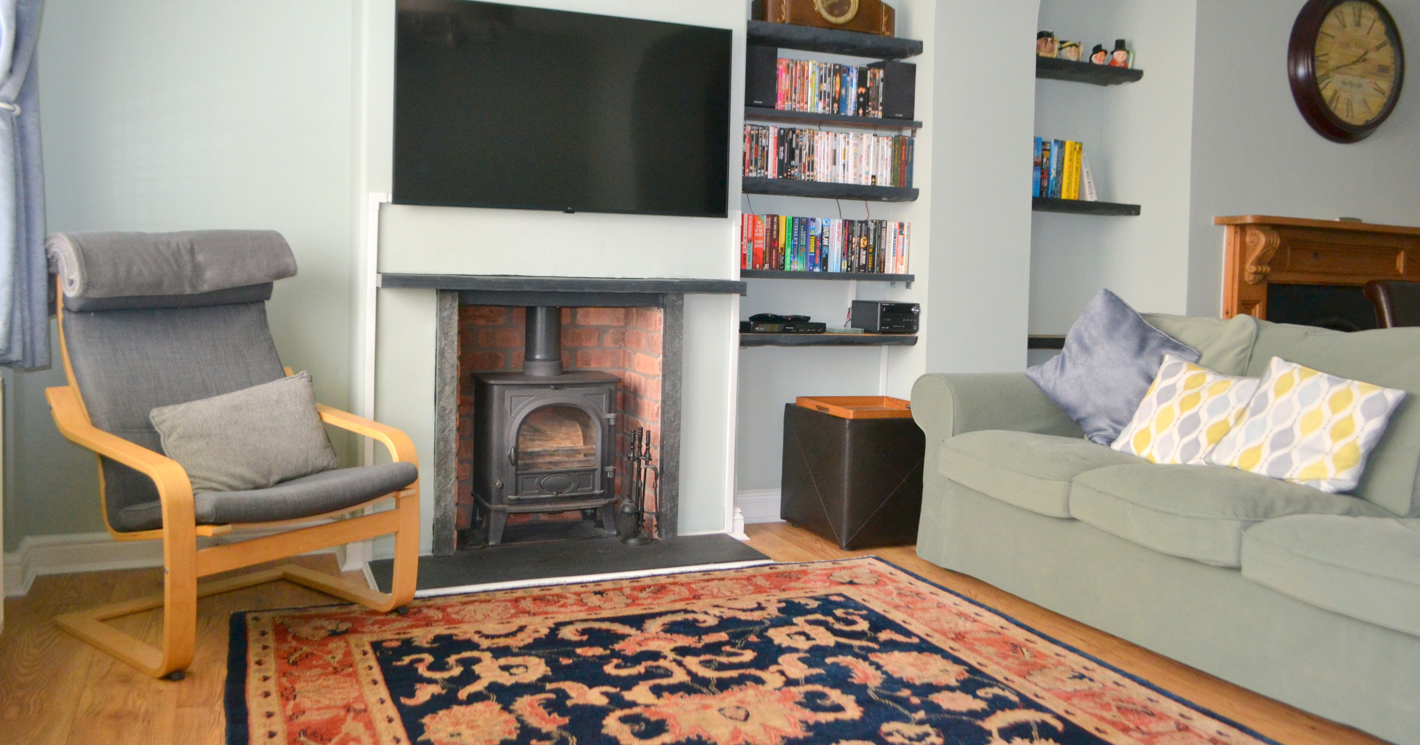 Modern living room with a wood burner, armchair, bookshelf, television, and sofa