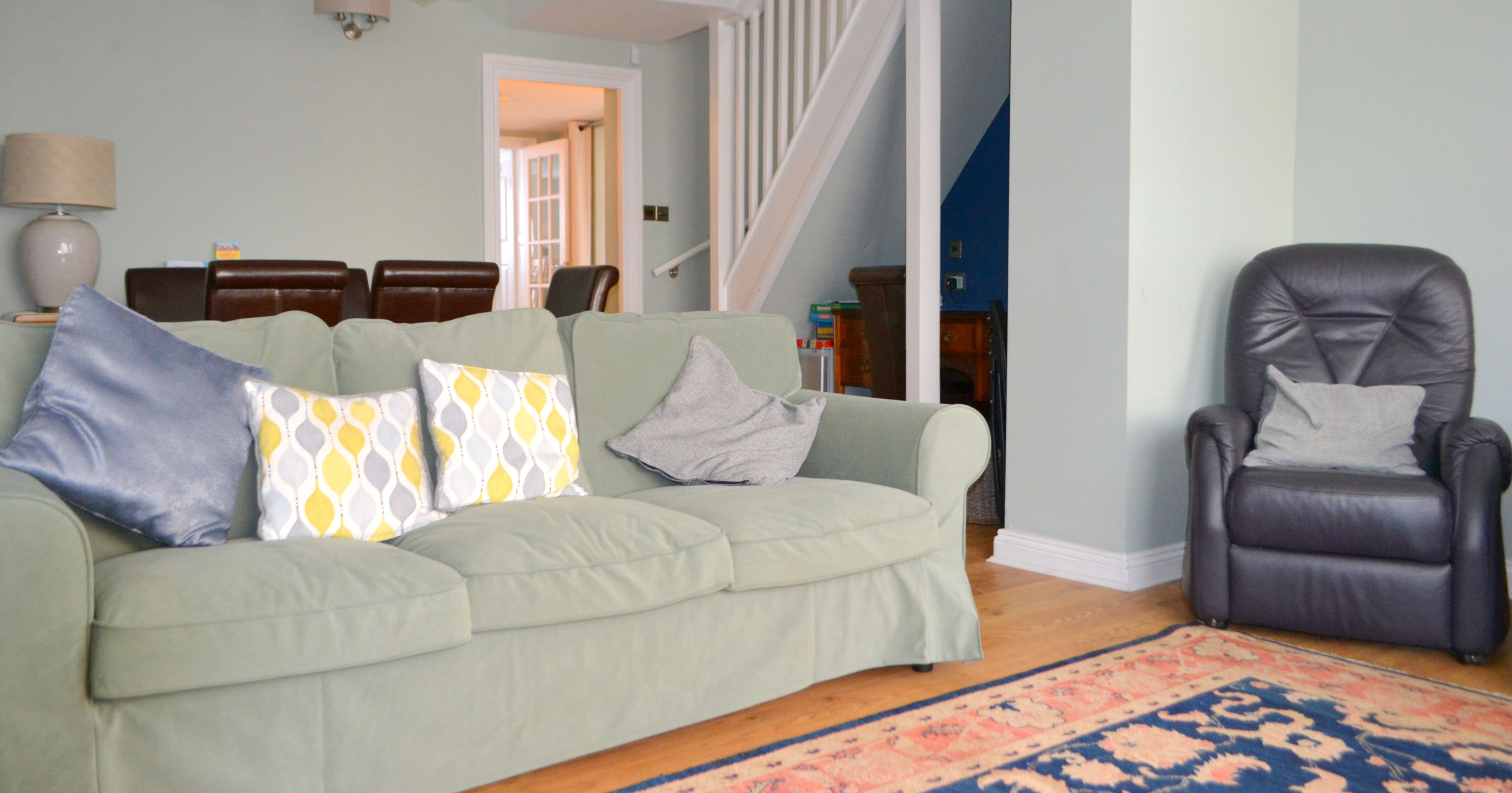 Living room with green sofa, colorful cushions, black armchair, dining area, and staircase