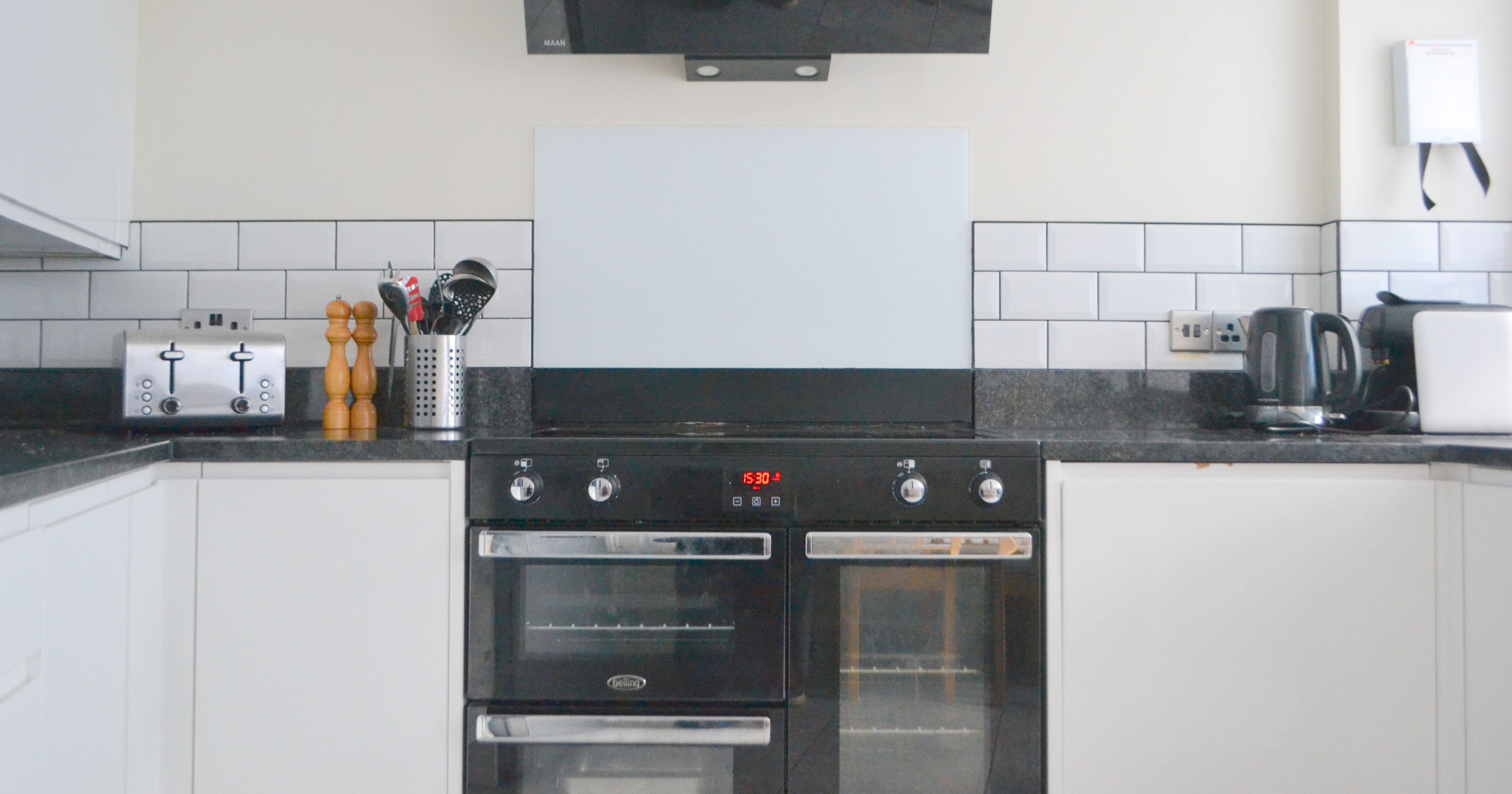 Modern kitchen oven with black glass hood, surrounded by white cabinets and countertop appliances.