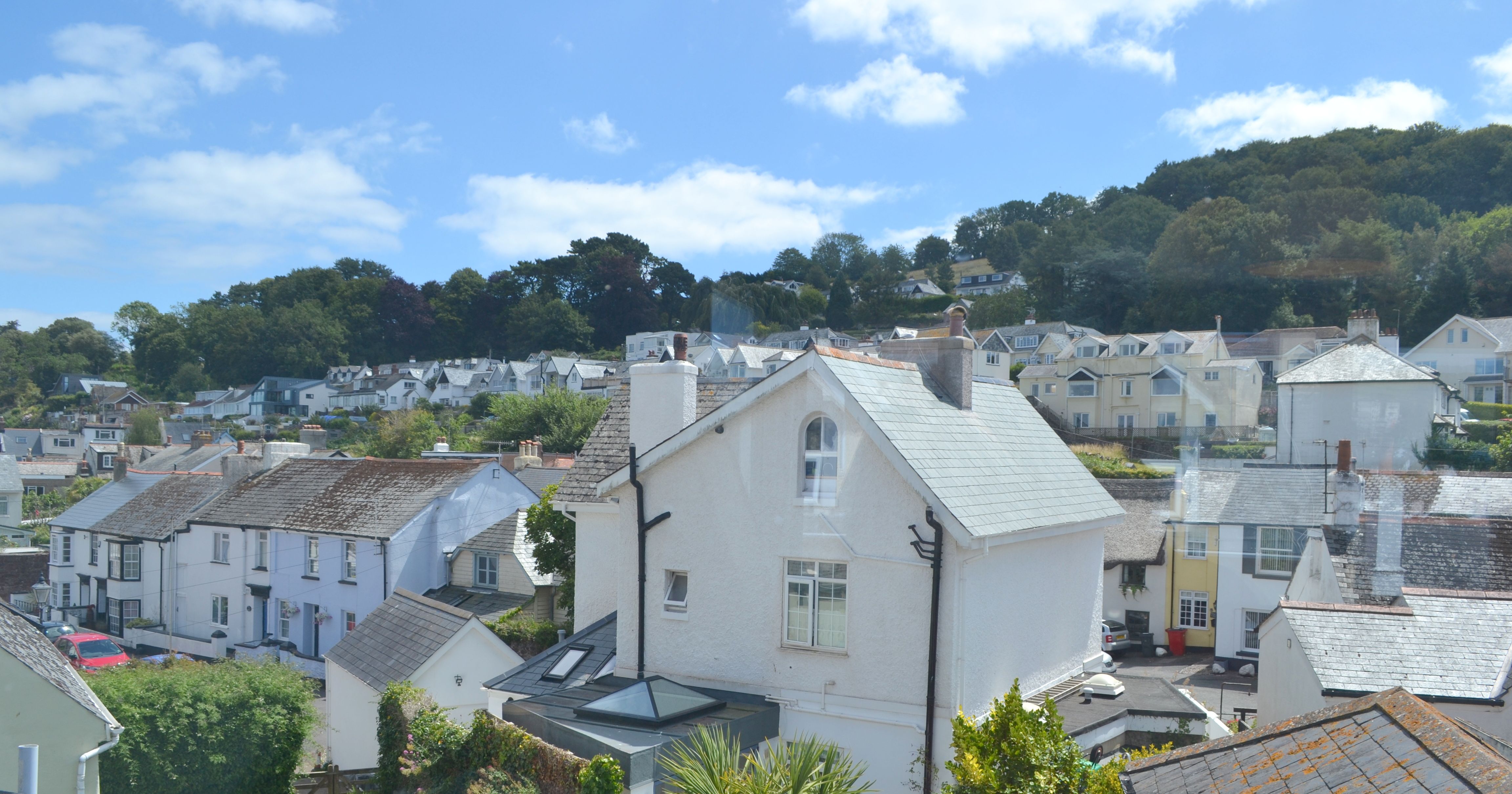 View of a hillside village with white and pastel-colored houses and green trees under a blue sky.