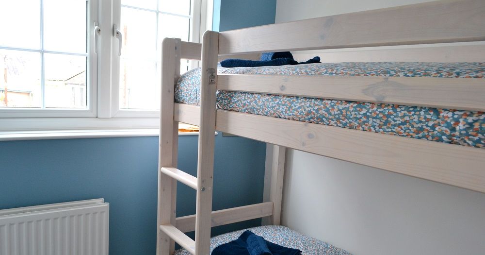 Wooden bunk beds with patterned bedding next to a window in a blue-walled room.