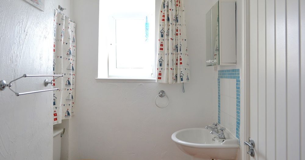 Bright family bathroom with nautical-themed curtains, a white sink, and blue tile accents.