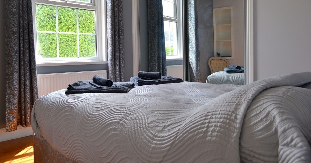 Modern double bedroom on the first floor with a large window, mirror-fronted wardrobe, and neatly made bed with folded towels on top.