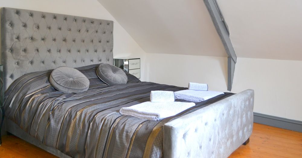 Large upholstered bed with gray bedding in a modern attic bedroom.