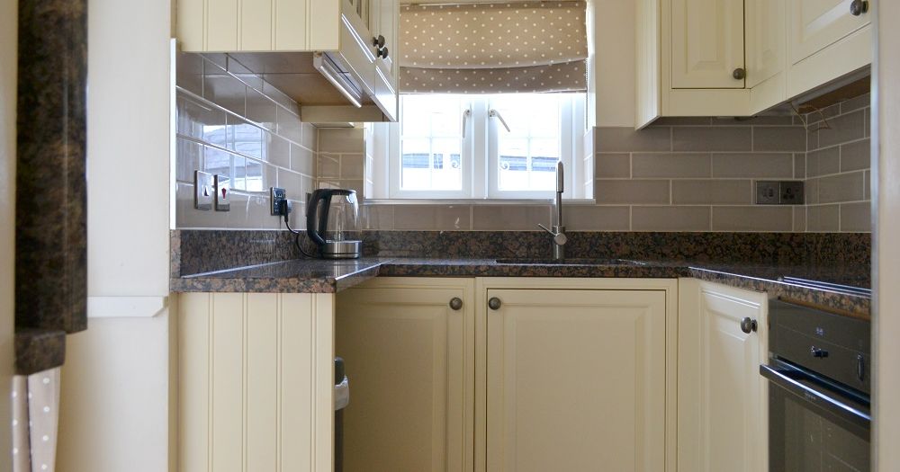 Compact modern kitchen with cream cabinets, black countertops, and a window above the sink.