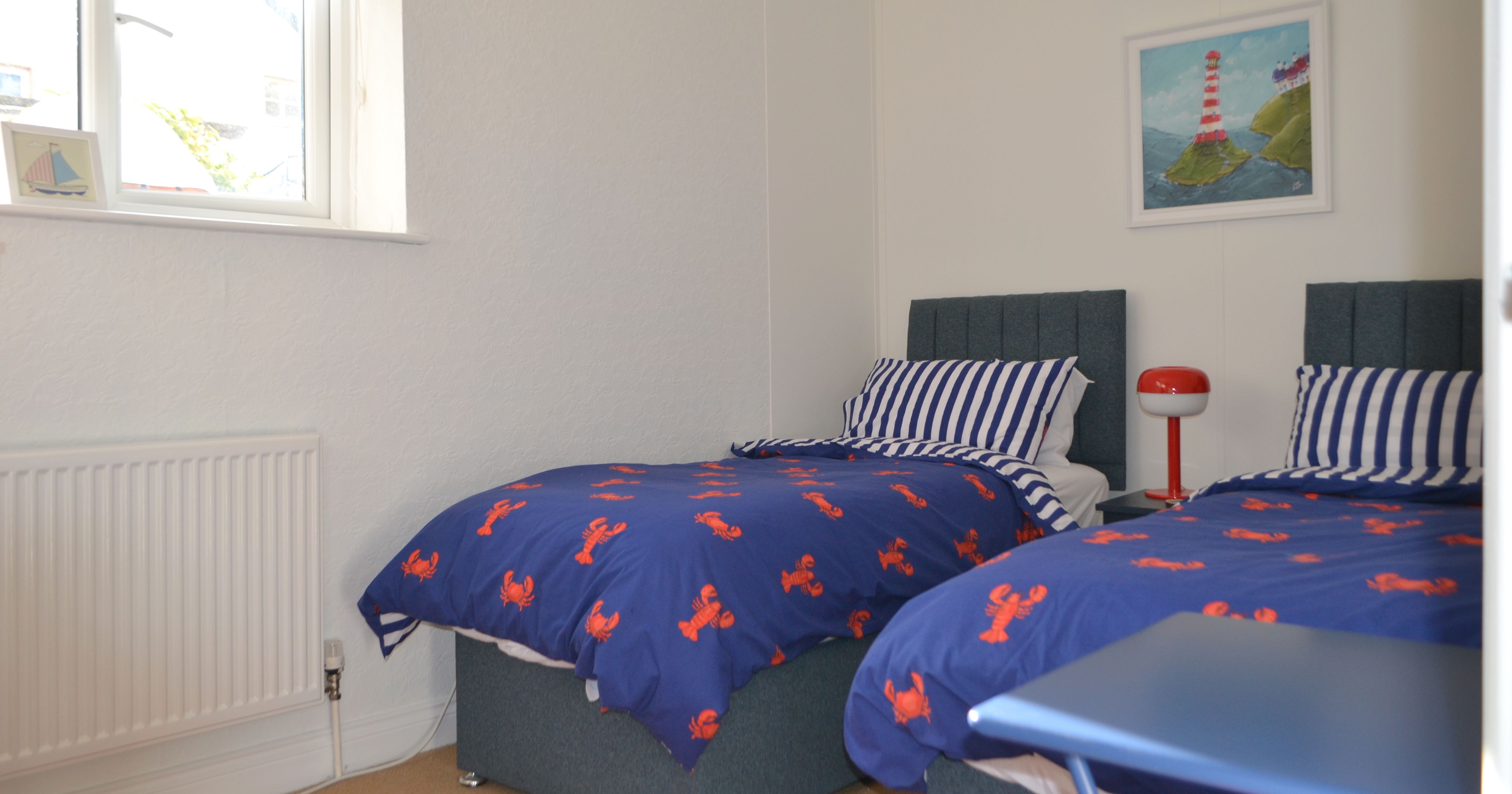 Bedroom with two single beds, blue bedding with red lobsters, and striped pillows