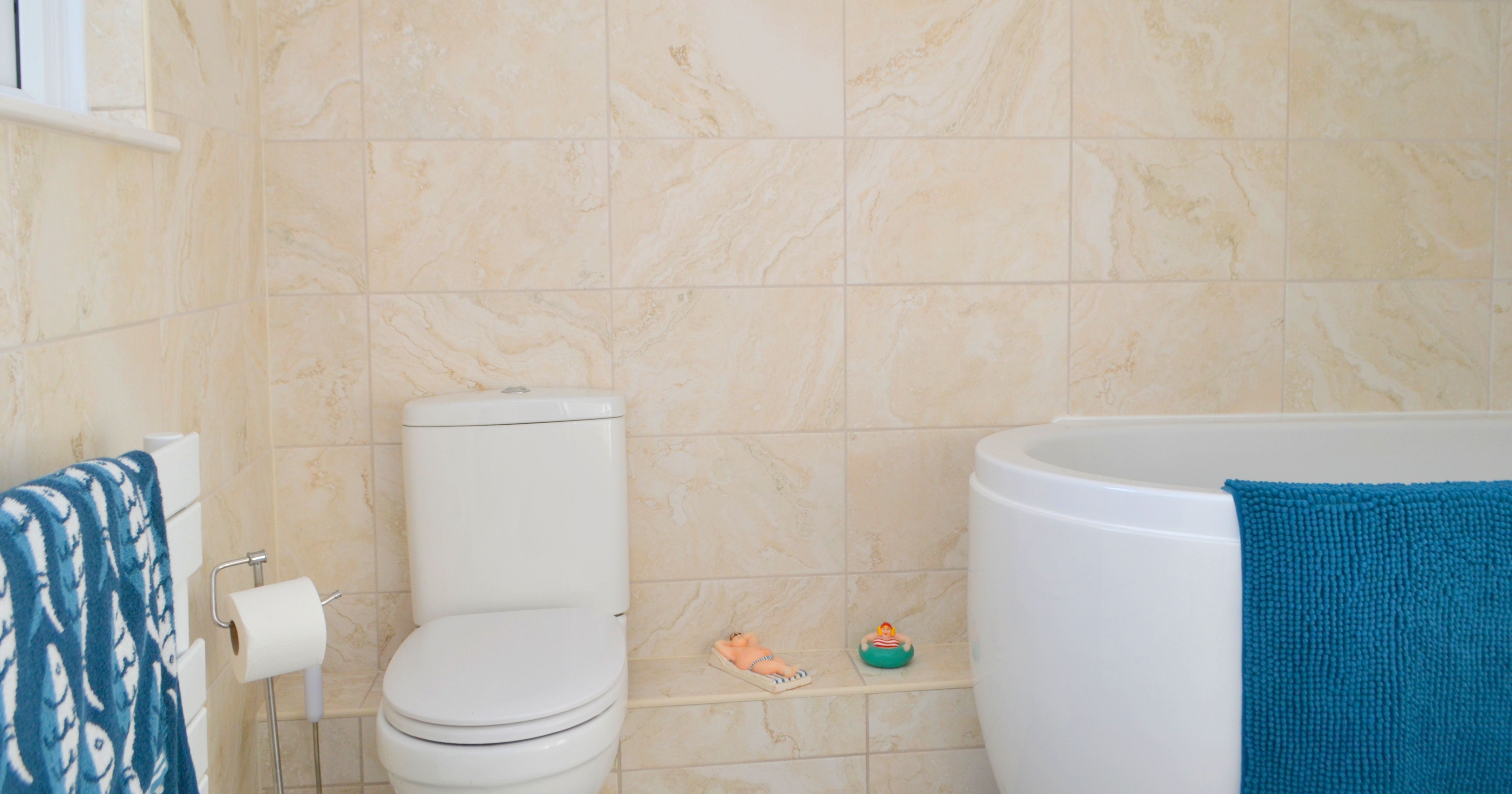 Modern bathroom with a white toilet, bathtub, blue towel, and beige tiles