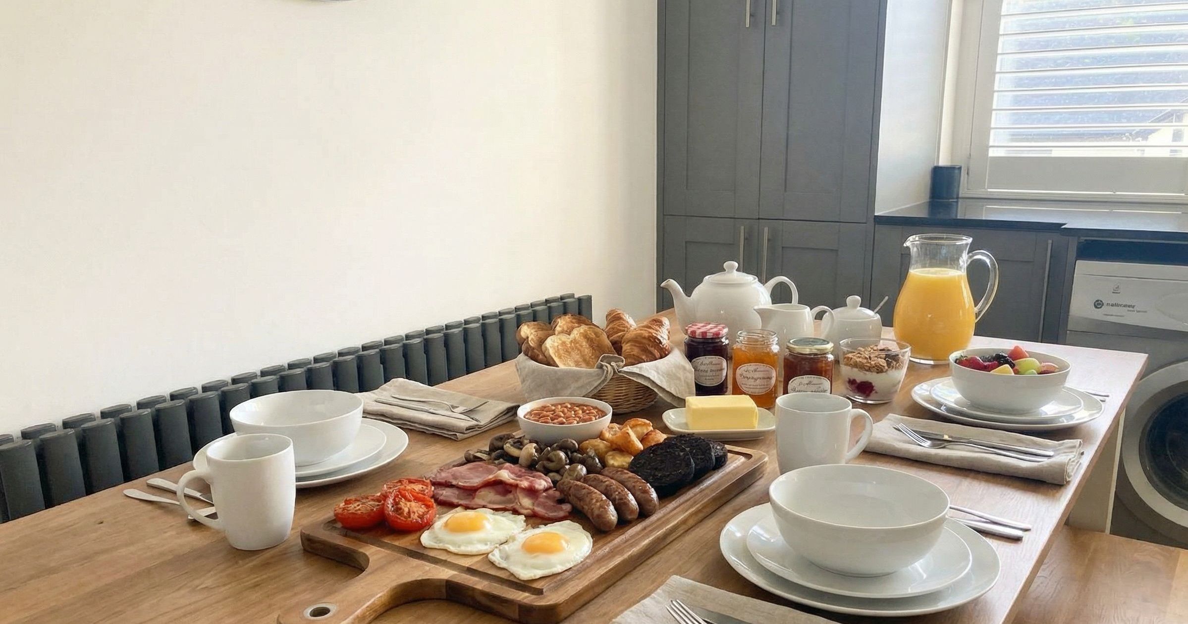 A breakfast table set with an assortment of traditional English breakfast items, fruit, juice, and pastries.