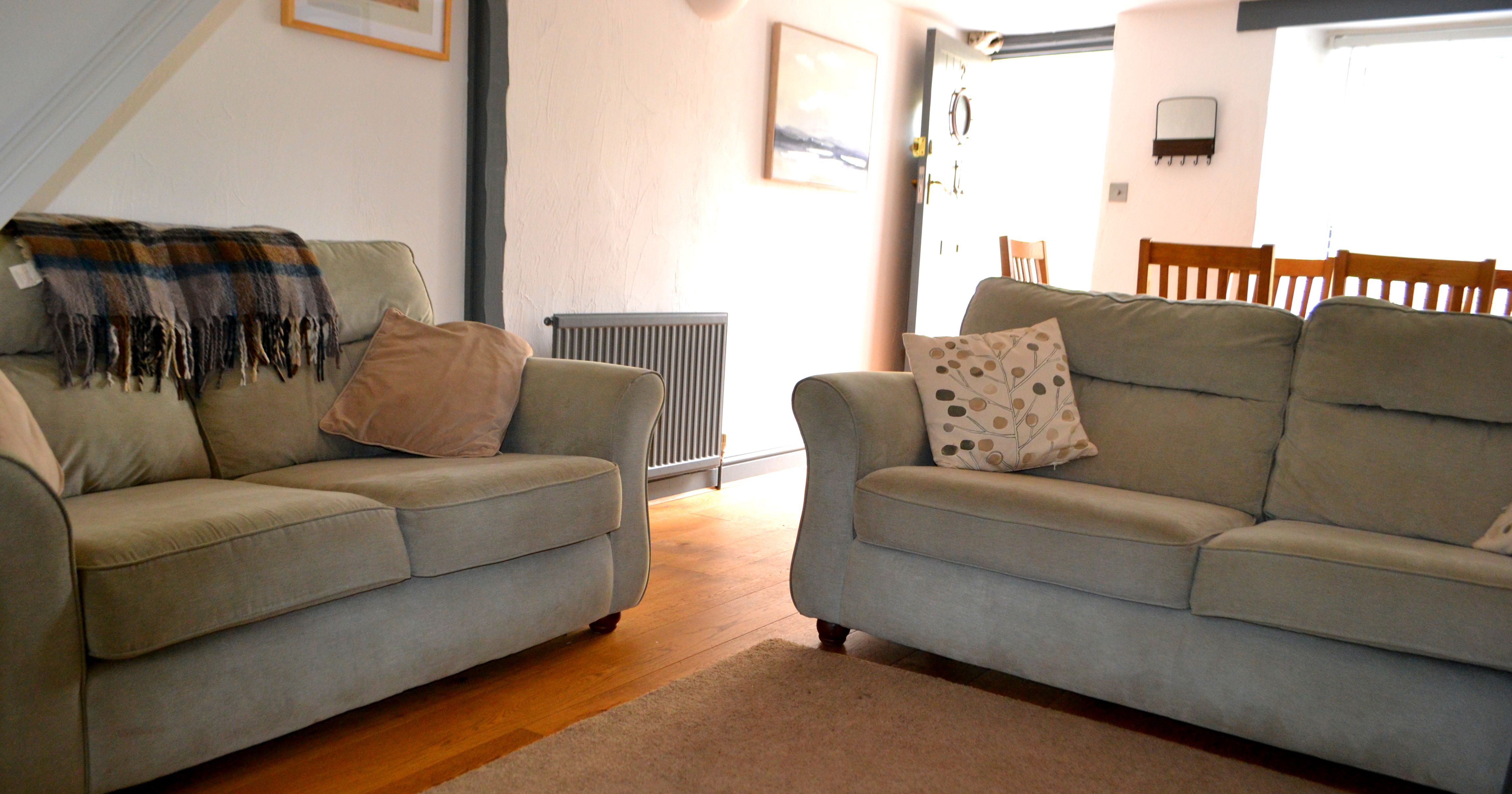 Cozy living room with two light green sofas, patterned pillows, a throw blanket, and wooden flooring.