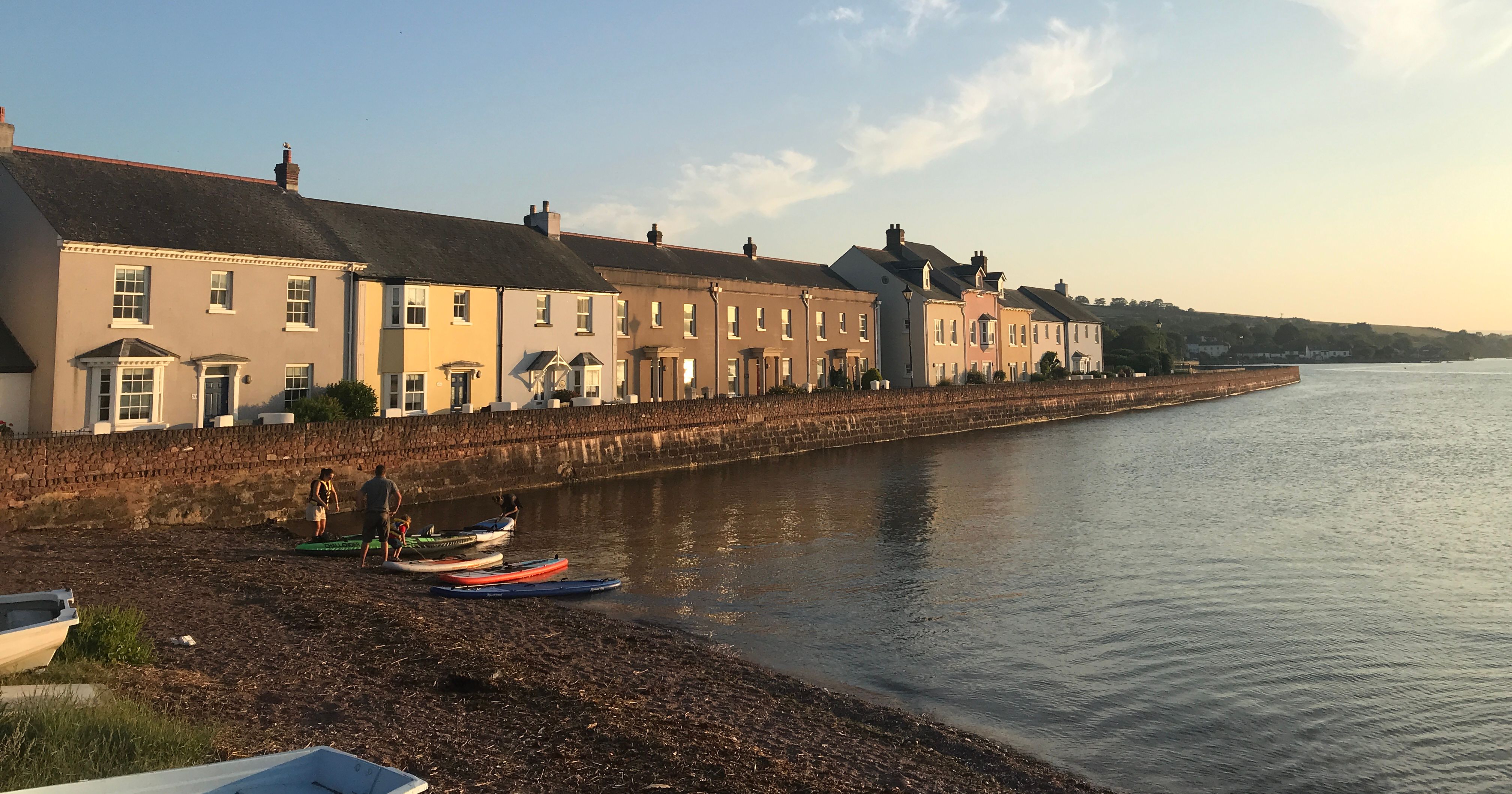Row of colorful houses along the shoreside of River Teign in Shaldon during sunset.