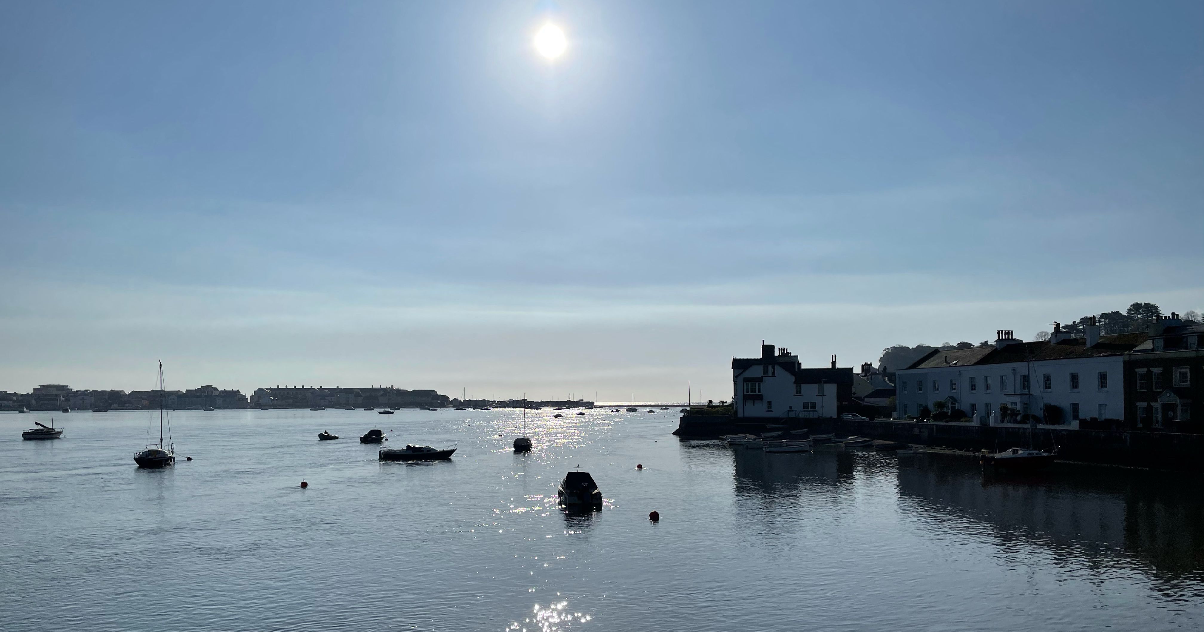 Boats floating on a calm river near houses under a bright sun.