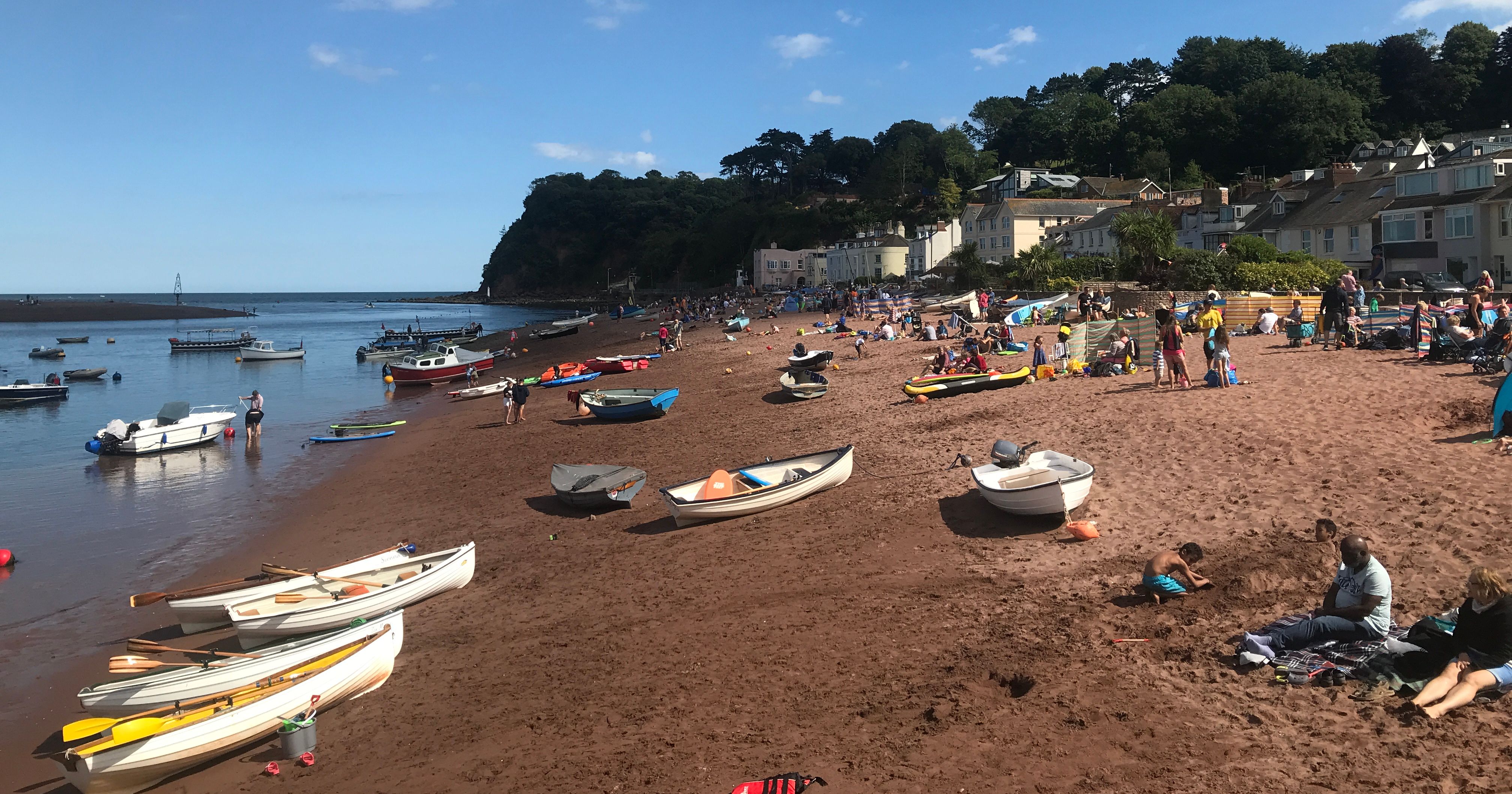 People relaxing and boats on the sandy Shaldon Beach under a blue sky