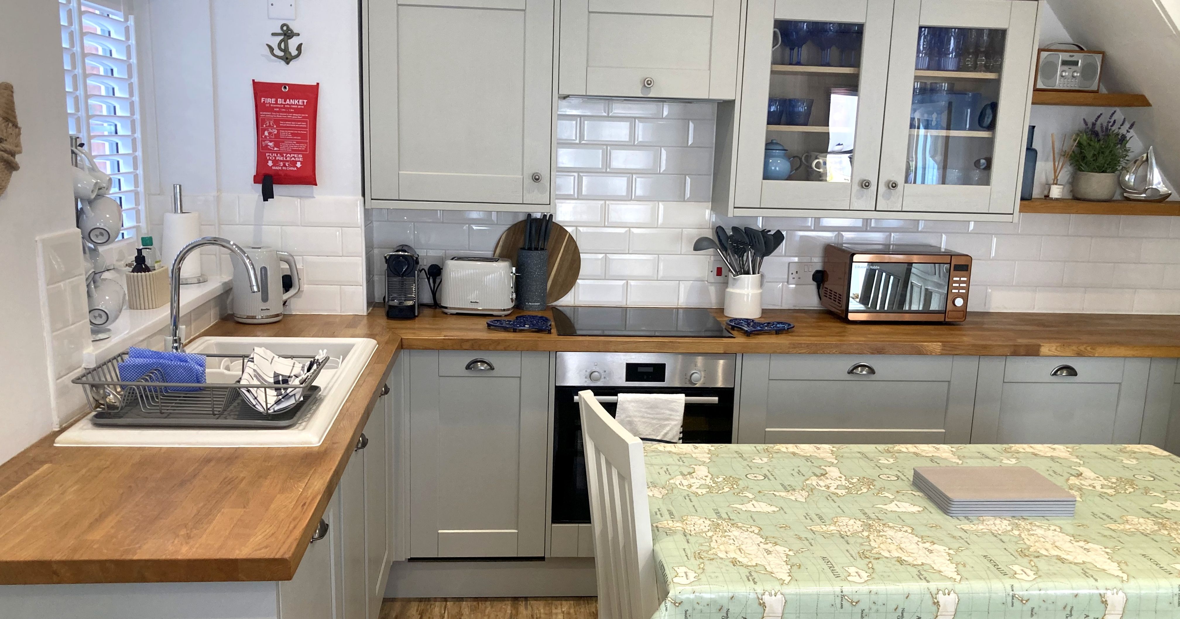 Modern kitchen with light gray cabinets, wooden countertops, and a table covered with a map-patterned tablecloth.