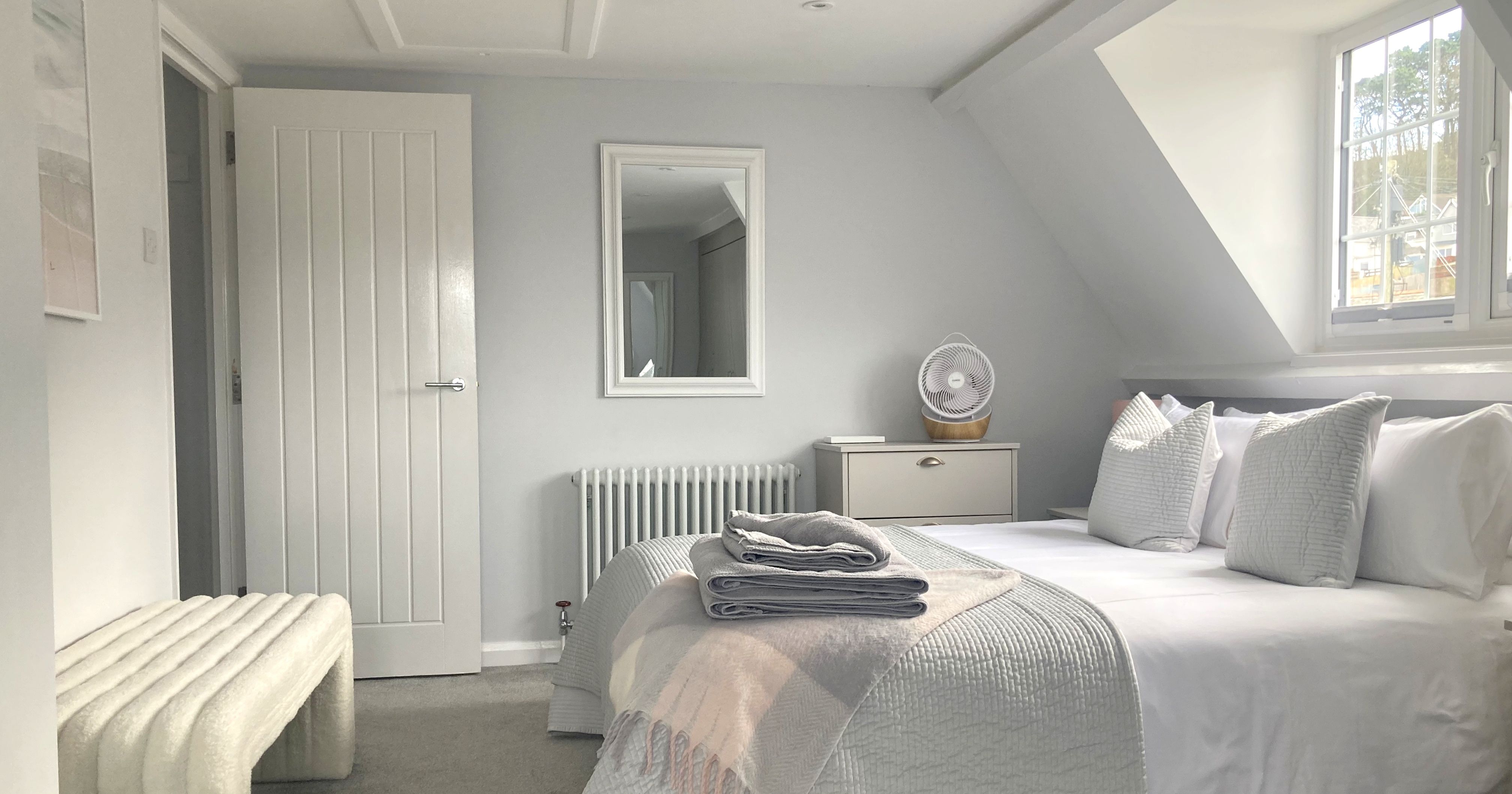 Bright modern bedroom with king size bed, stacked towels, a mirror, and a window with natural light.