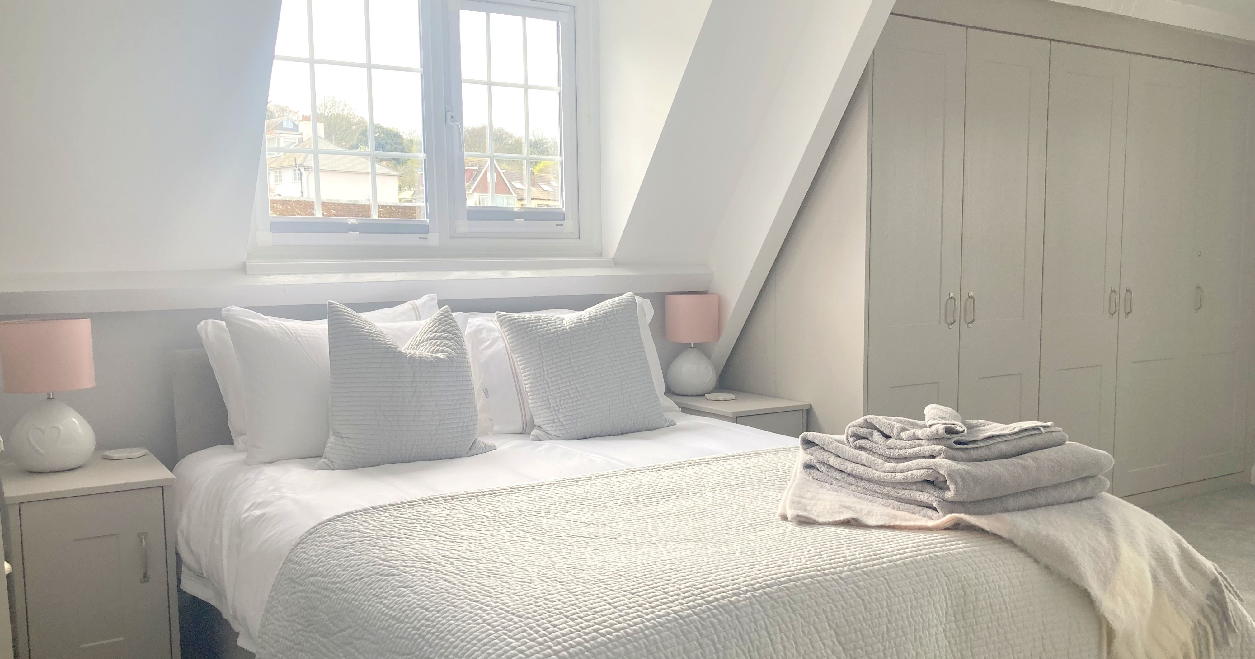 Bright master bedroom with king-sized bed, large wardrobe, and folded towels on the bed.