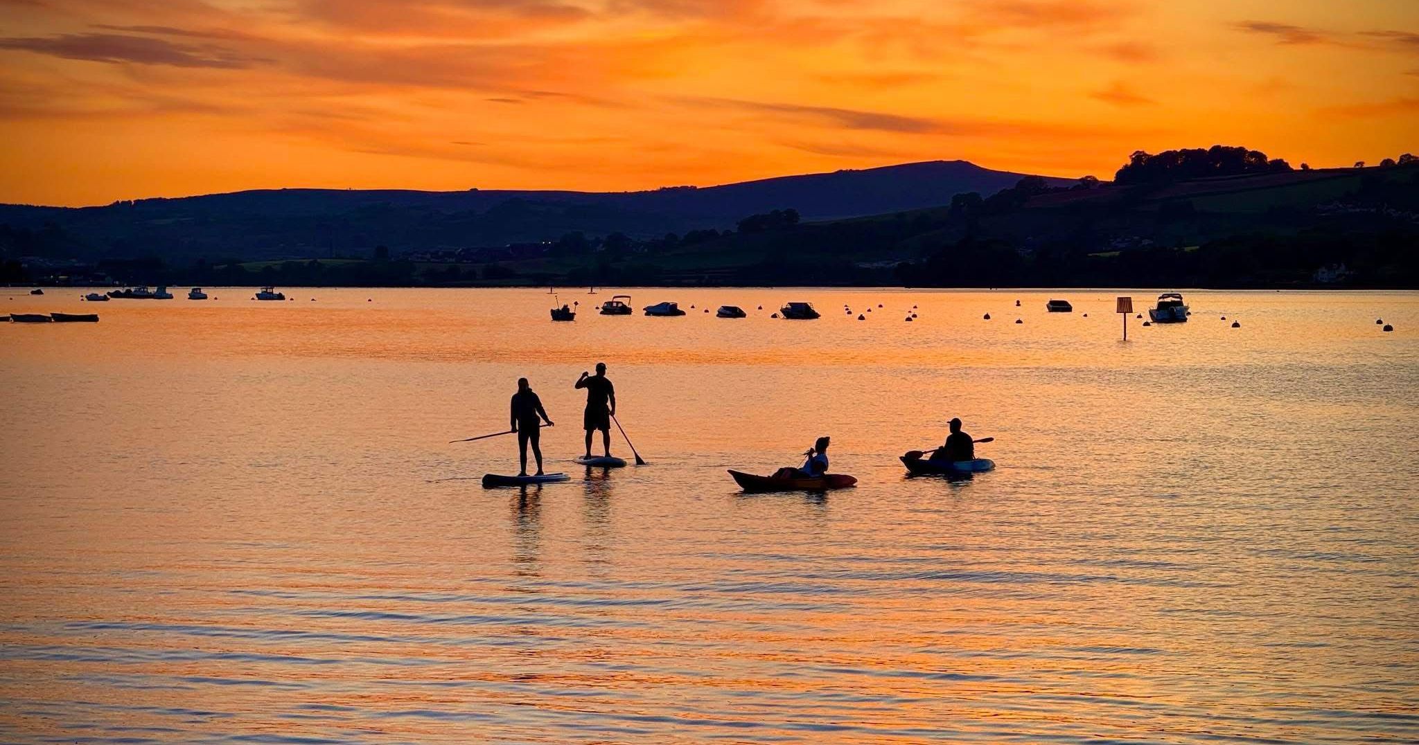 Silhouettes of kayakers and paddle boarders on the River Teign at sunset