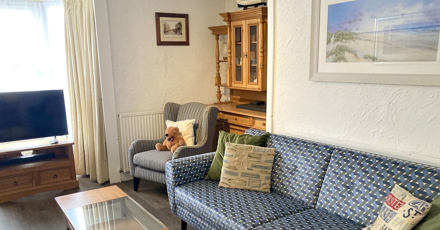 Cozy living room with patterned blue sofa, striped armchair with teddy bear, wooden furniture, and beach-themed decor.