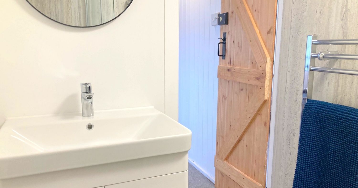 Modern bathroom with a white sink, round mirror, wooden door, and navy blue towel
