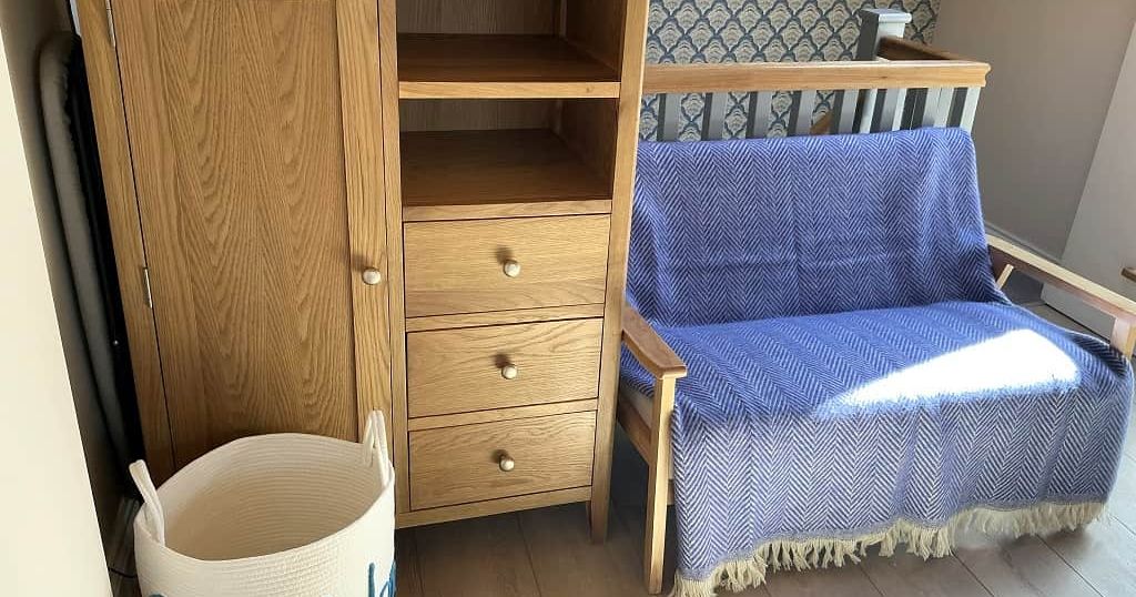Wooden cabinet with drawers, small wooden sofa with blue blanket, and a white basket with 'Shaldon' written on it.