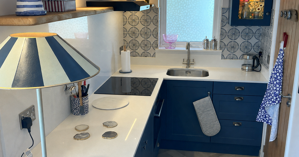 Modern small kitchen with blue cabinets, striped lampshade, patterned backsplash, and countertop appliances.