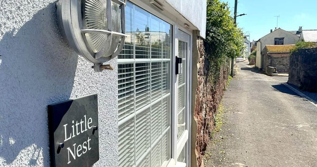 Exterior of a building with a sign that reads 'Little Nest' next to a window, and a narrow lane running alongside the building.