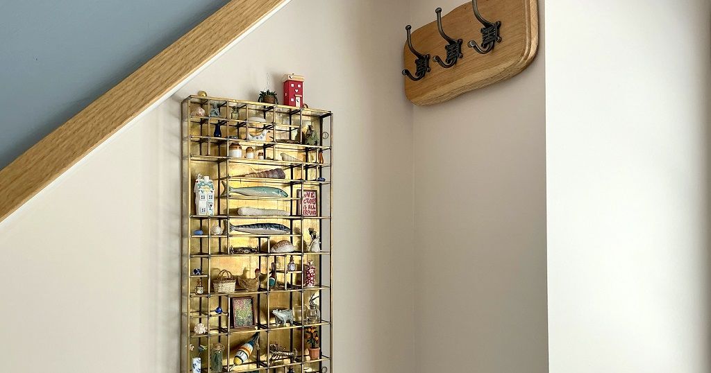 Wall-mounted wooden display case with miniatures beside a coat rack with three hooks under a sloped ceiling.